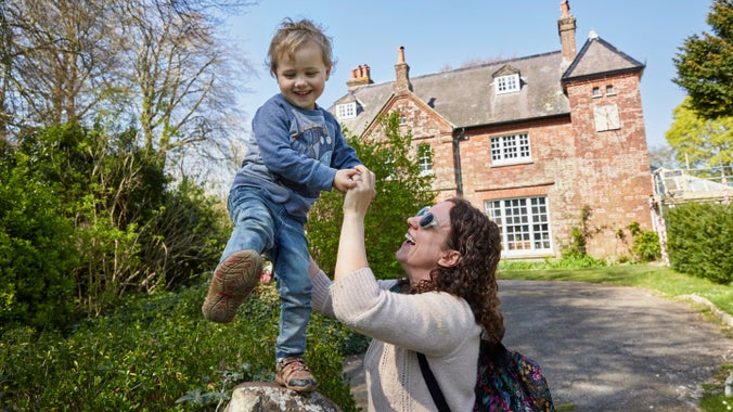 Smiling child standing on a rock held by his mother in the garden at Max Gate, Dorset